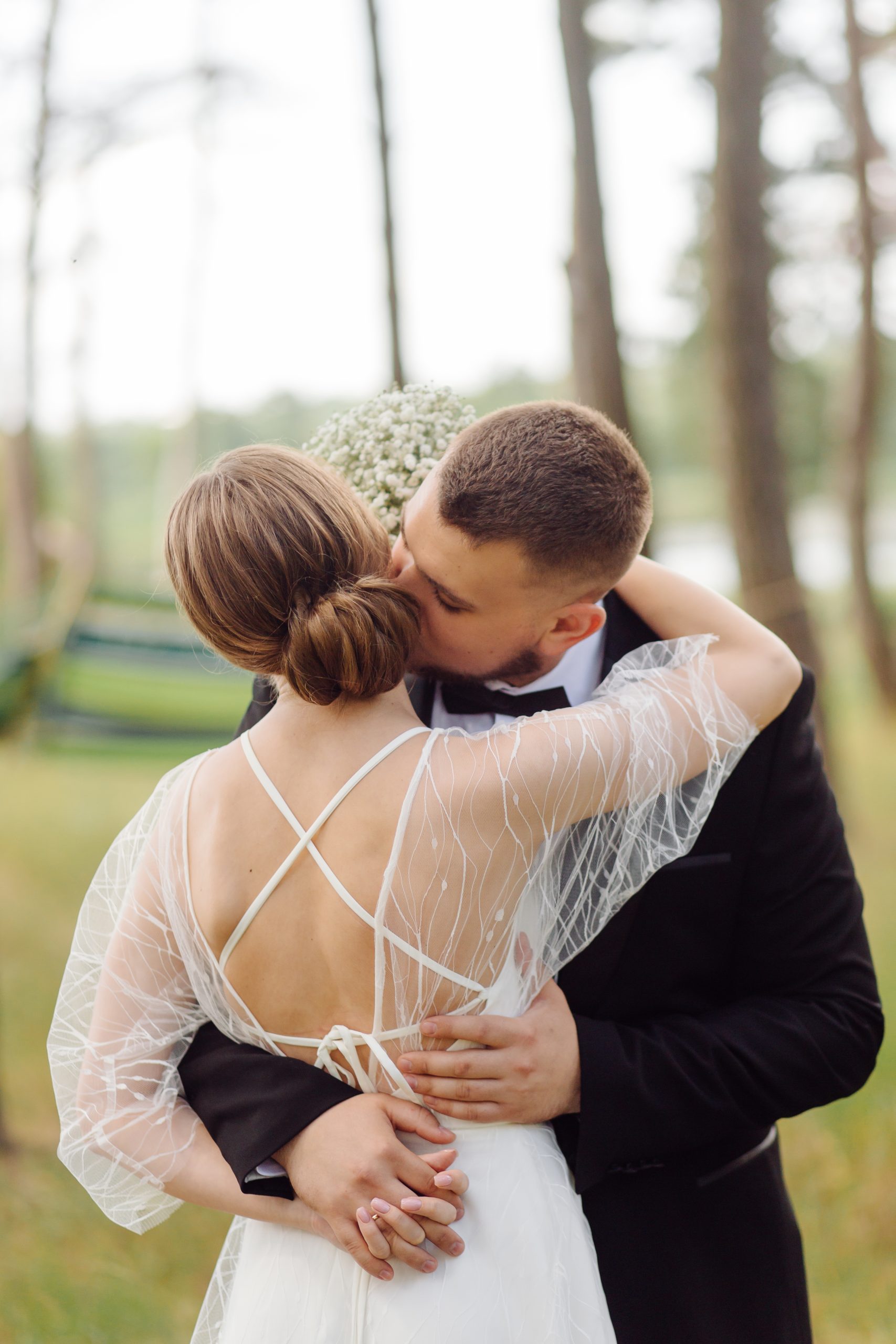 Wedding portrait of the newlyweds. A bearded, stylish groom in a suit and a beautiful blonde bride in a white dress with a bouquet in her hands are standing and hugging in nature in the pine forest. Wedding portrait of the newlyweds. A bearded, stylish groom in a suit and a beautiful blonde bride in a white dress with a bouquet in her hands are standing and hugging in nature in the pine forest.